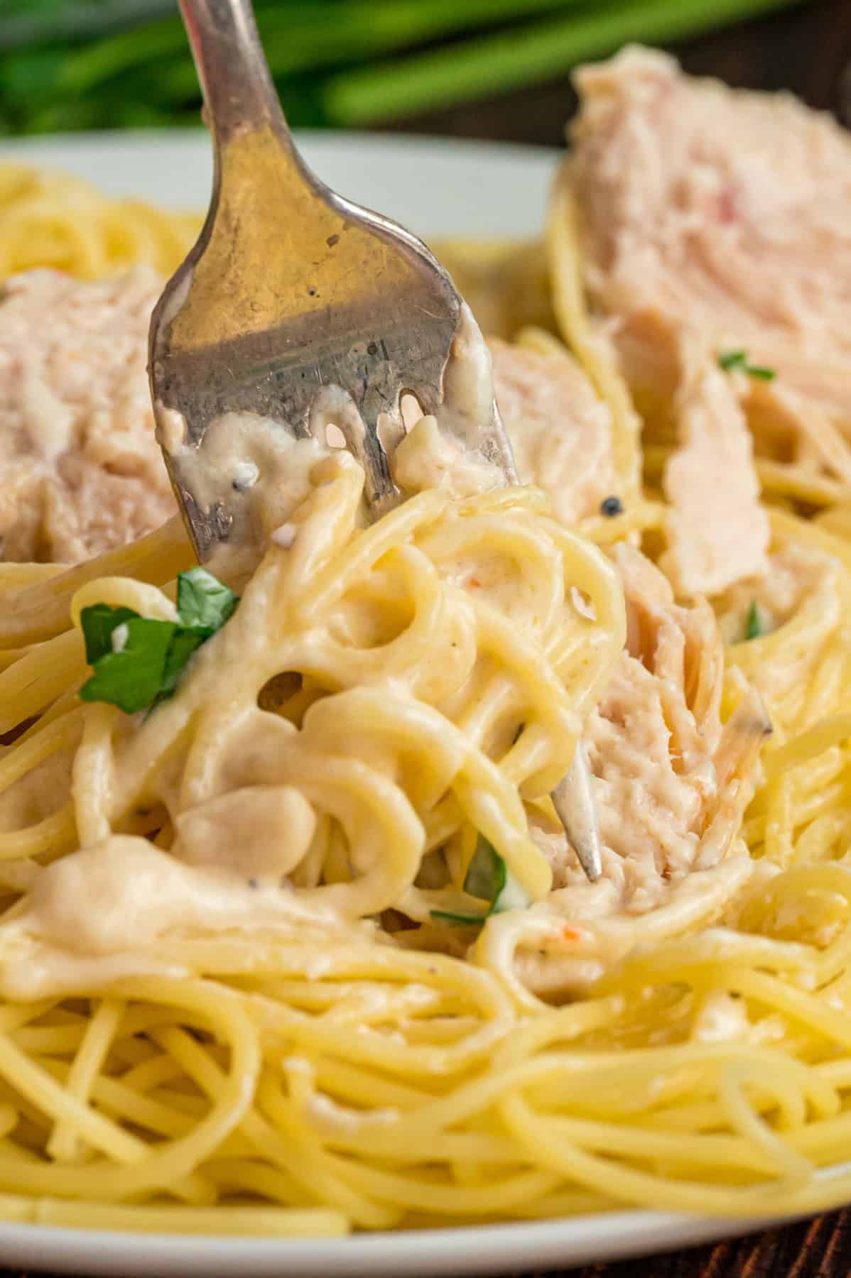 Chicken breasts are slow-cooked in a creamy sauce and served over pasta in this Angel Chicken recipe. A family favorite! A fork swirling angel chicken pasta