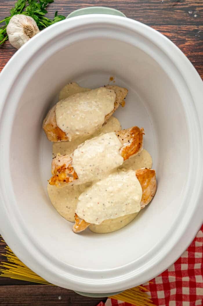 Chicken breasts are slow-cooked in a creamy sauce and served over pasta in this Angel Chicken recipe. A family favorite! Seared chicken breasts in a crockpot topped with creamy sauce