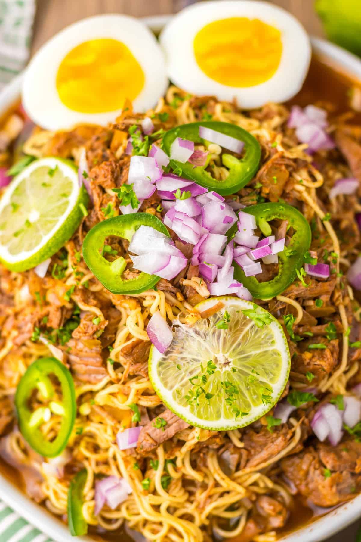 Tender birria beef slow cooks all day before getting tossed with ramen noodles and toppings in this Birria Ramen recipe. A bowl of birria ramen topped with jalapeno, onion, and lime slices