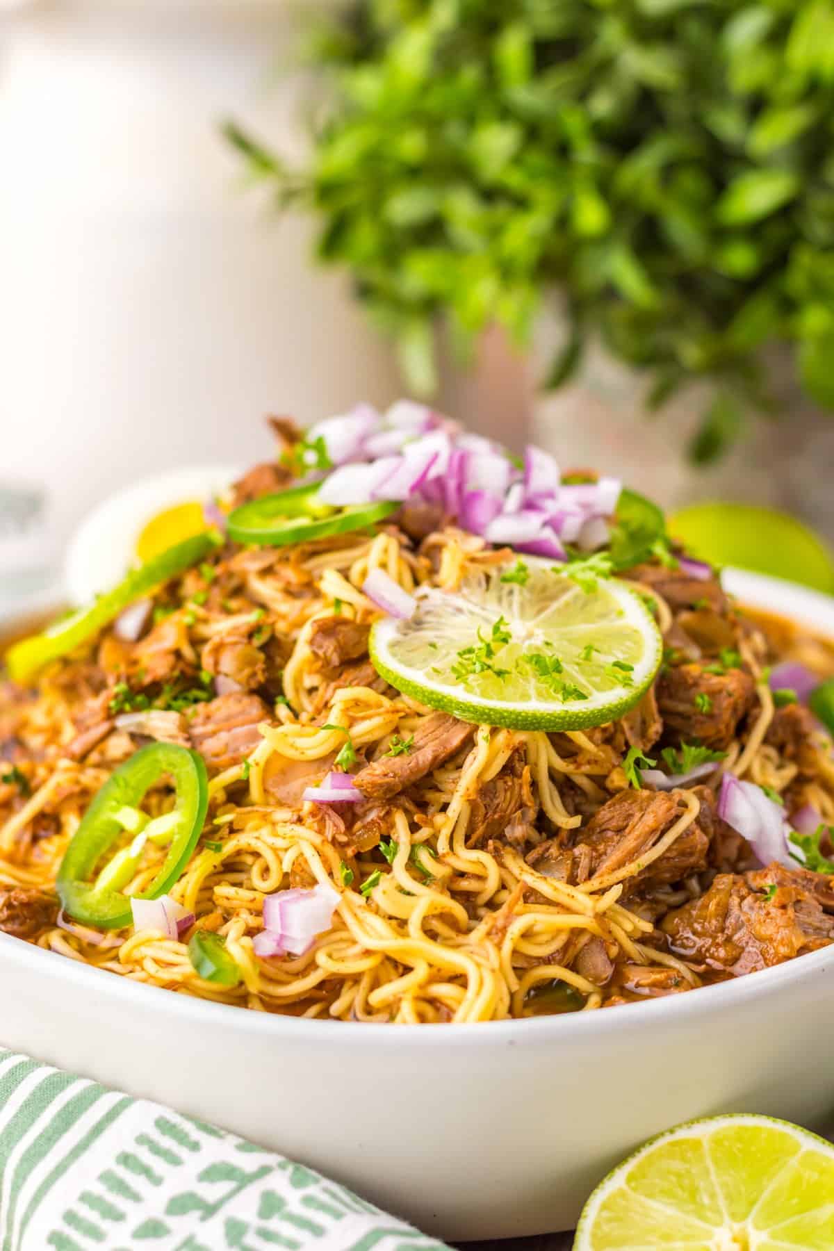 Tender birria beef slow cooks all day before getting tossed with ramen noodles and toppings in this Birria Ramen recipe. Side view of a bowl of birria ramen with lime and jalapeno slices