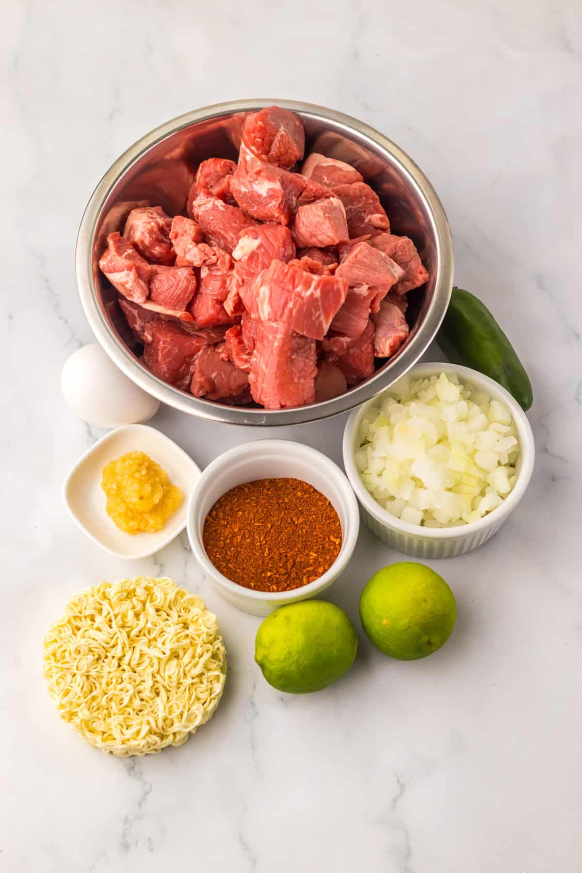 Tender birria beef slow cooks all day before getting tossed with ramen noodles and toppings in this Birria Ramen recipe. Overhead view of ingredients needed to make birria ramen