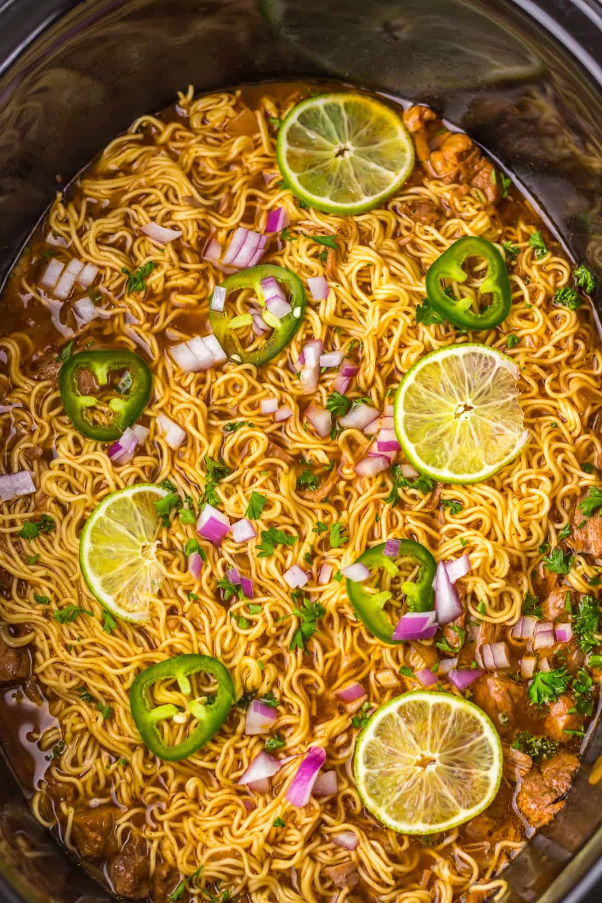 Tender birria beef slow cooks all day before getting tossed with ramen noodles and toppings in this Birria Ramen recipe. Birria ramen in a slow cooker topped with jalapeno and lime slices