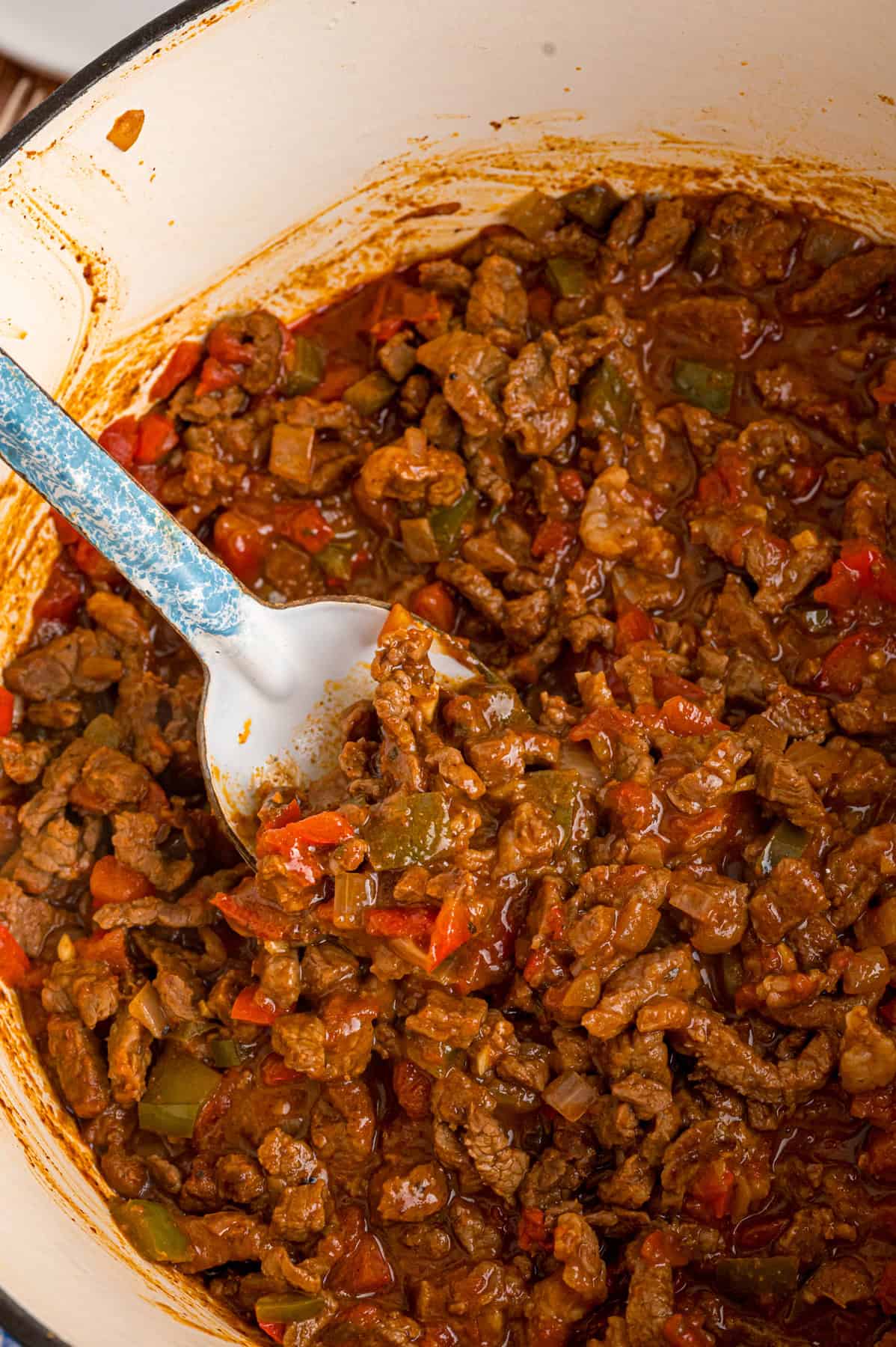 This Carne Picada recipe features braised beef and veggies in a rich, savory sauce. Serve with rice and beans or in tacos and burrito bowls. A spoon in a bowl of carne picada