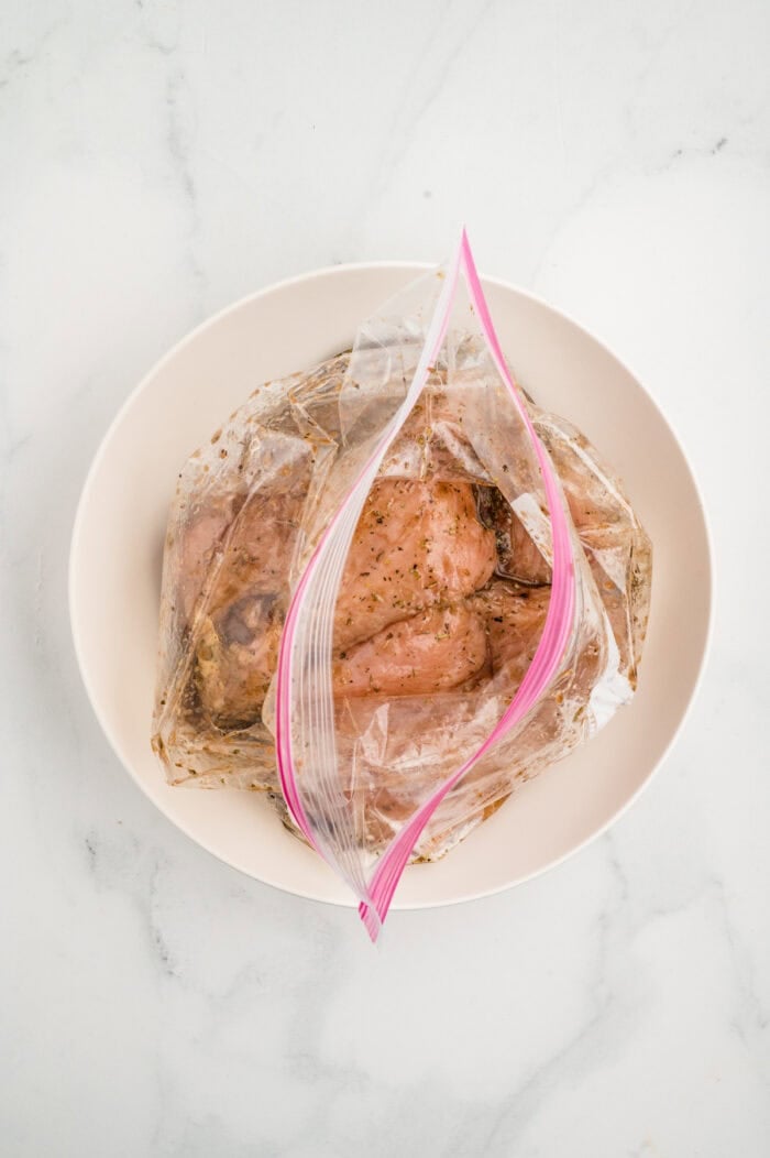 Grilled chicken breasts are topped with marinated balsamic tomatoes, fresh mozzarella, and basil in this easy Chicken Caprese recipe. Chicken marinating in a ziploc bag