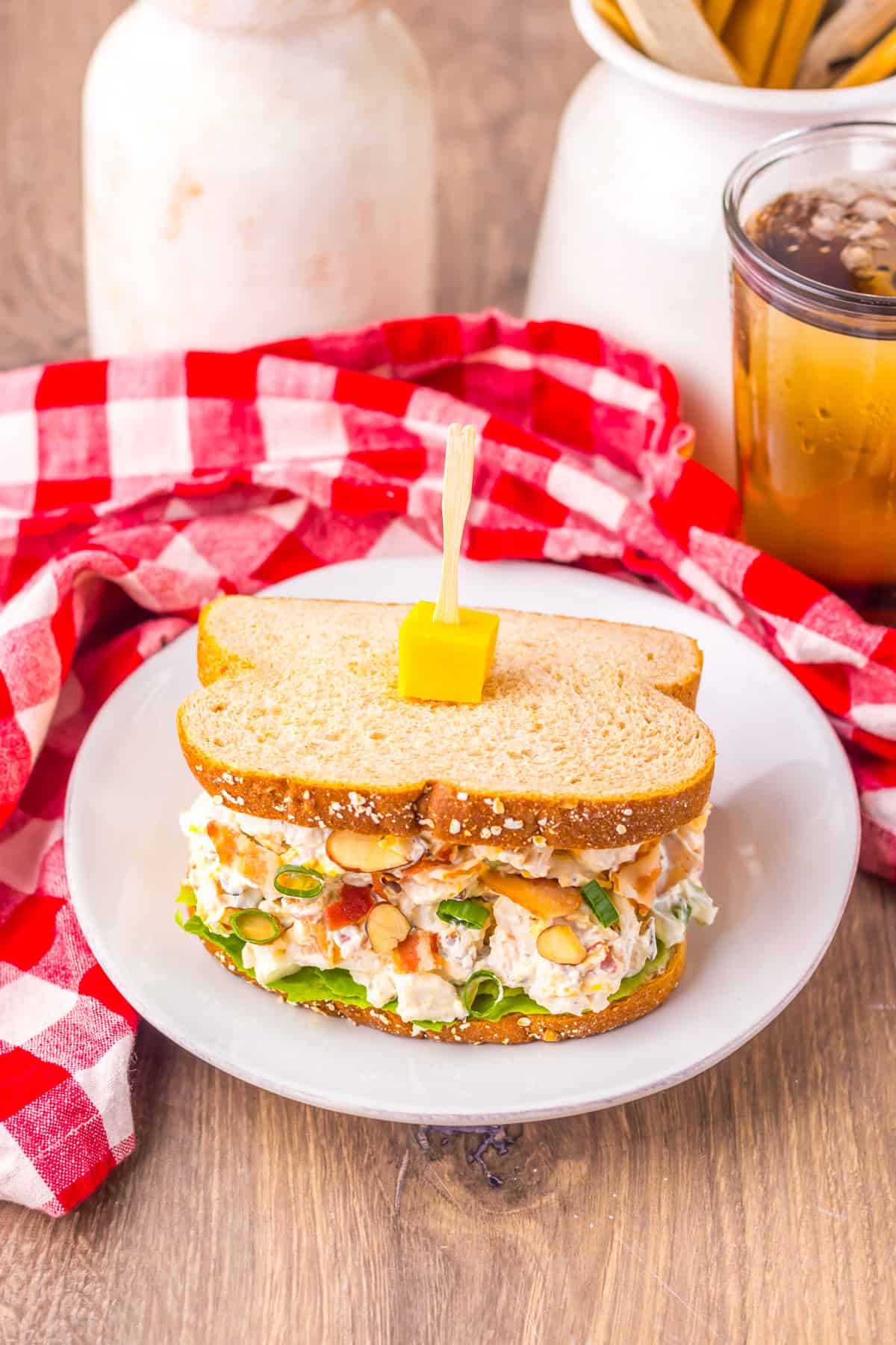 If you love chicken salad, this Million Dollar Chicken Salad with Bacon is a must-try! It’s rich, savory, and creamy with just the right amount of crunch, loaded with crispy bacon, and with balanced flavors that make it taste like a million bucks in every bite. Top-down view of a chicken salad sandwich on a white plate, placed on a wooden table with a red checkered napkin and a glass of iced tea in the background.
