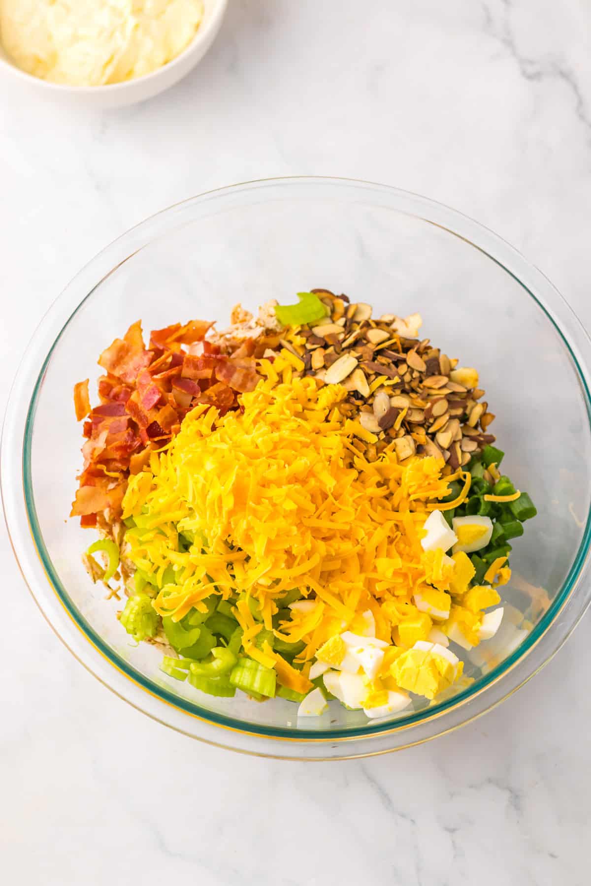 If you love chicken salad, this Million Dollar Chicken Salad with Bacon is a must-try! It’s rich, savory, and creamy with just the right amount of crunch, loaded with crispy bacon, and with balanced flavors that make it taste like a million bucks in every bite. Bowl of ingredients for chicken salad including chopped bacon, shredded cheddar, celery, green onions, and chopped hard-boiled eggs, ready to be mixed with dressing.