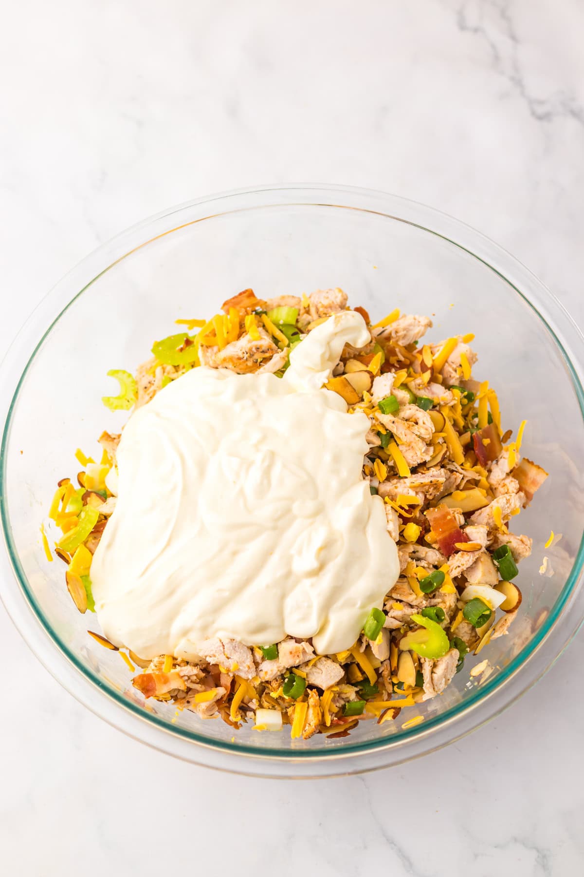 If you love chicken salad, this Million Dollar Chicken Salad with Bacon is a must-try! It’s rich, savory, and creamy with just the right amount of crunch, loaded with crispy bacon, and with balanced flavors that make it taste like a million bucks in every bite. Glass mixing bowl filled with chicken, cheese, green onions, celery, and bacon, topped with a dollop of creamy dressing ready to be mixed.