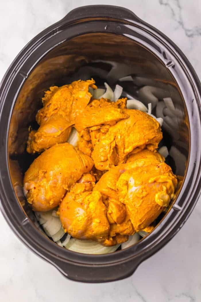 Marinated chicken thighs slow cook until tender in this Chicken Shawarma recipe. Serve piled high on pita with veggies & yogurt sauce. Marinated chicken thighs on top of onion slices in the slow cooker