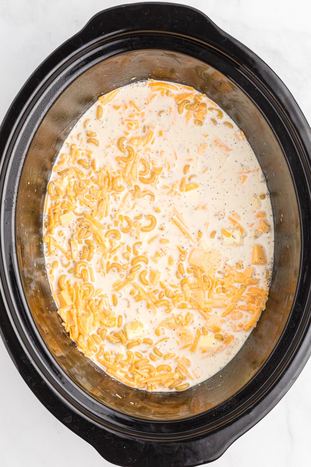 Made with a mix of cheddar and American cheeses, this Crock Pot Mac and Cheese is uber creamy and super easy to make. Overhead view of slow cooker mac and cheese ready to be cooked