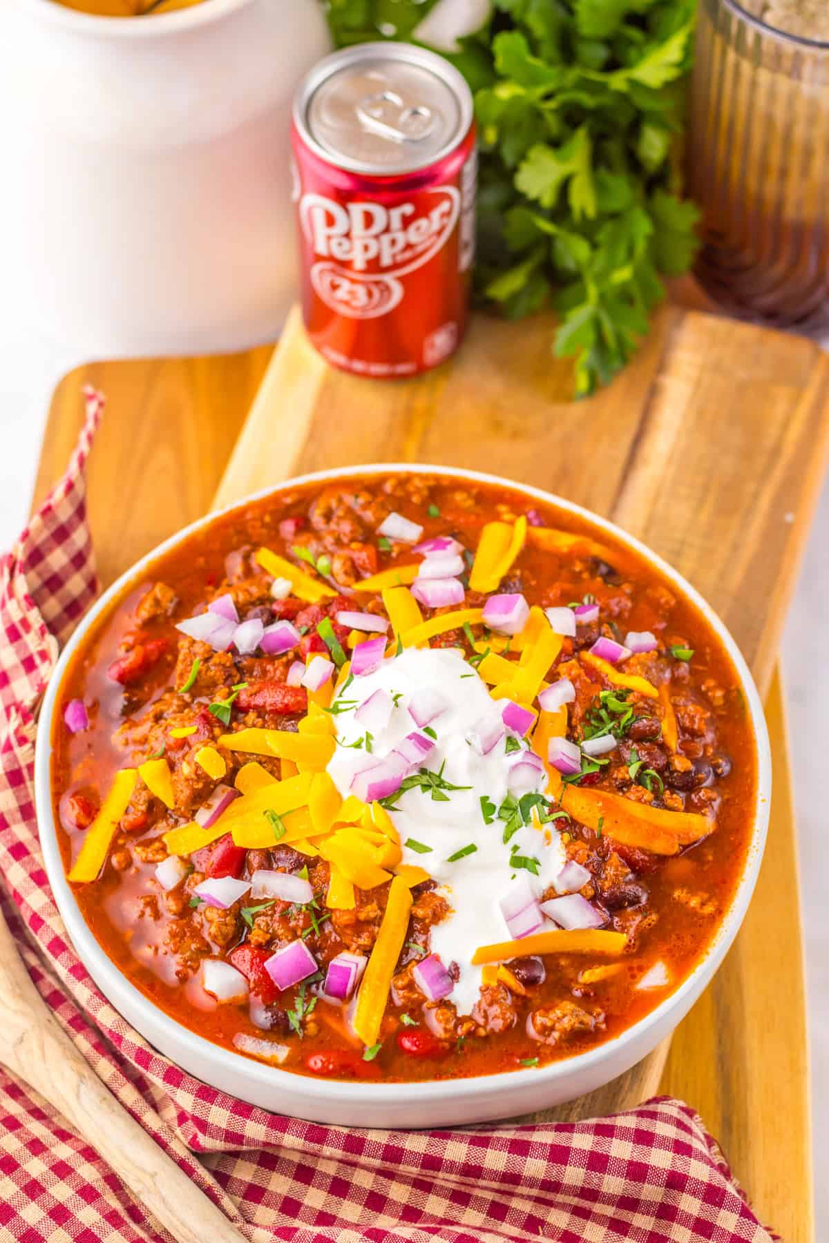 This sweet and tangy Dr. Pepper Chili is a delicious slow cooker recipe that’s perfect for a weeknight dinner. cutting board with bowl on top filled with Dr. Pepper Chili