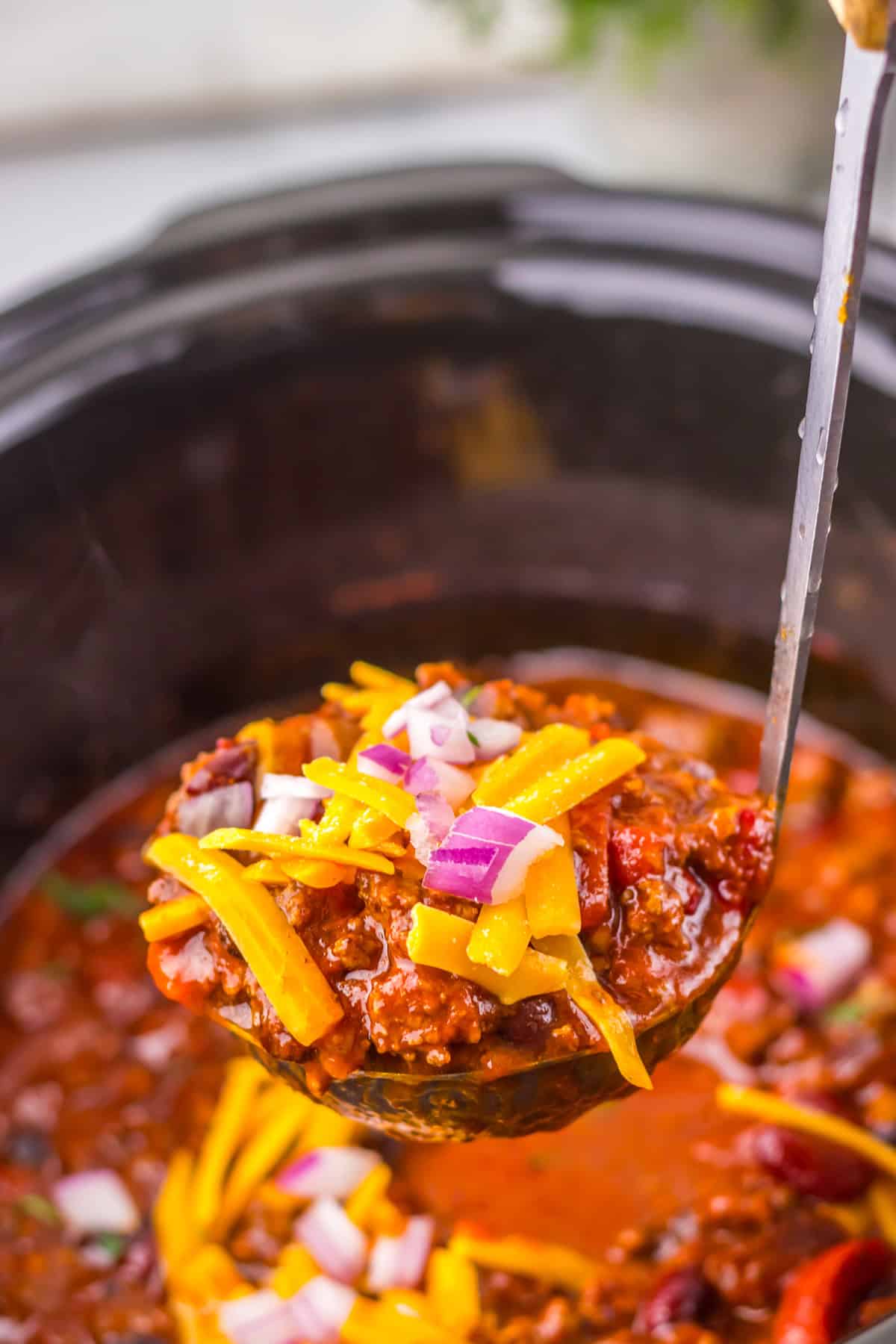 This sweet and tangy Dr. Pepper Chili is a delicious slow cooker recipe that’s perfect for a weeknight dinner. ladle with chili topped with red onion and cheese in slow cooker