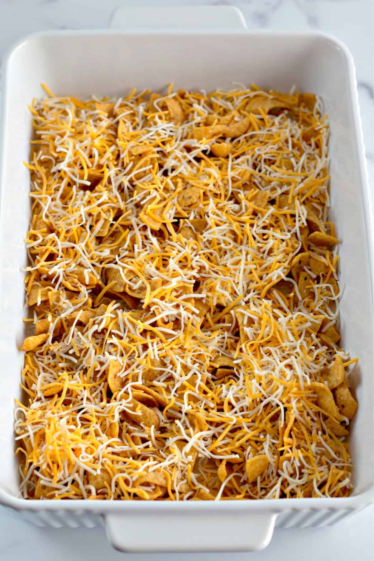 You'll love this Easy Frito Pie Recipe for a family-friendly dinner in a snap! shredded cheese on top of frito chips in a baking dish