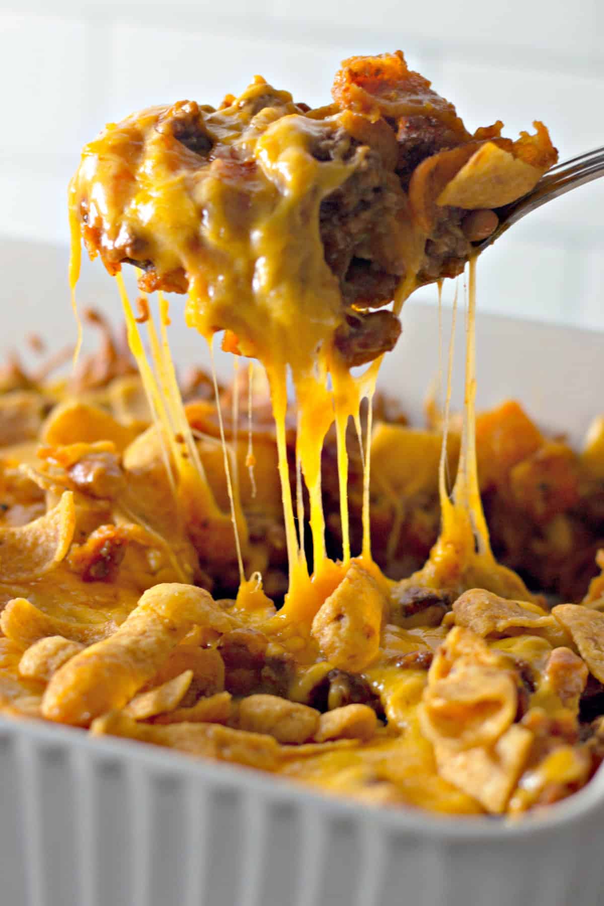 You'll love this Easy Frito Pie Recipe for a family-friendly dinner in a snap! lifting frito pie out of a baking dish with a spoon