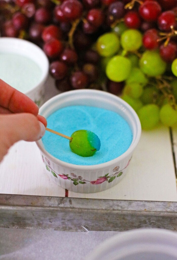 Candy Grapes are frozen grapes dipped and coated in a thin layer of vibrant and flavored Jello mix. dipping a grape into Jello