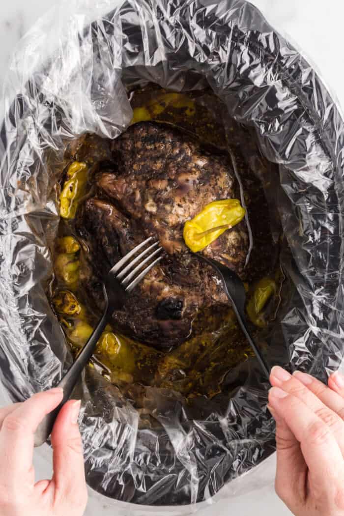Mississippi Pot Roast is a flavor explosion of slow-cooked chuck roast, ranch seasoning, au jus seasoning, pepperoncini, and butter. using forks to shred the roast