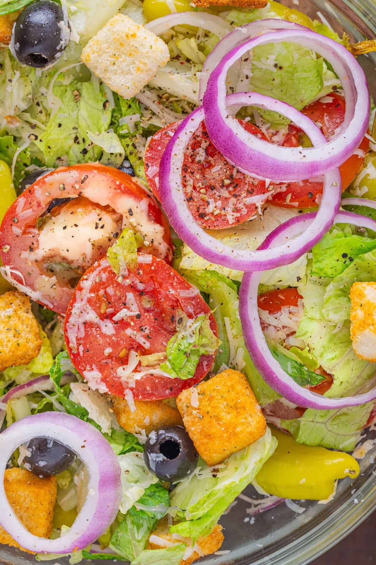 This Olive Garden Salad recipe features romaine lettuce hearts, pepperoncini, olives, and more tossed in a creamy Italian dressing. Close up of Olive Garden salad