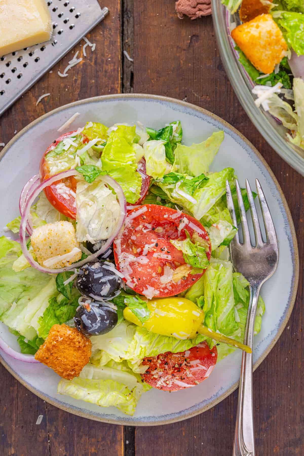 This Olive Garden Salad recipe features romaine lettuce hearts, pepperoncini, olives, and more tossed in a creamy Italian dressing. Overhead view of a plate of Olive Garden salad