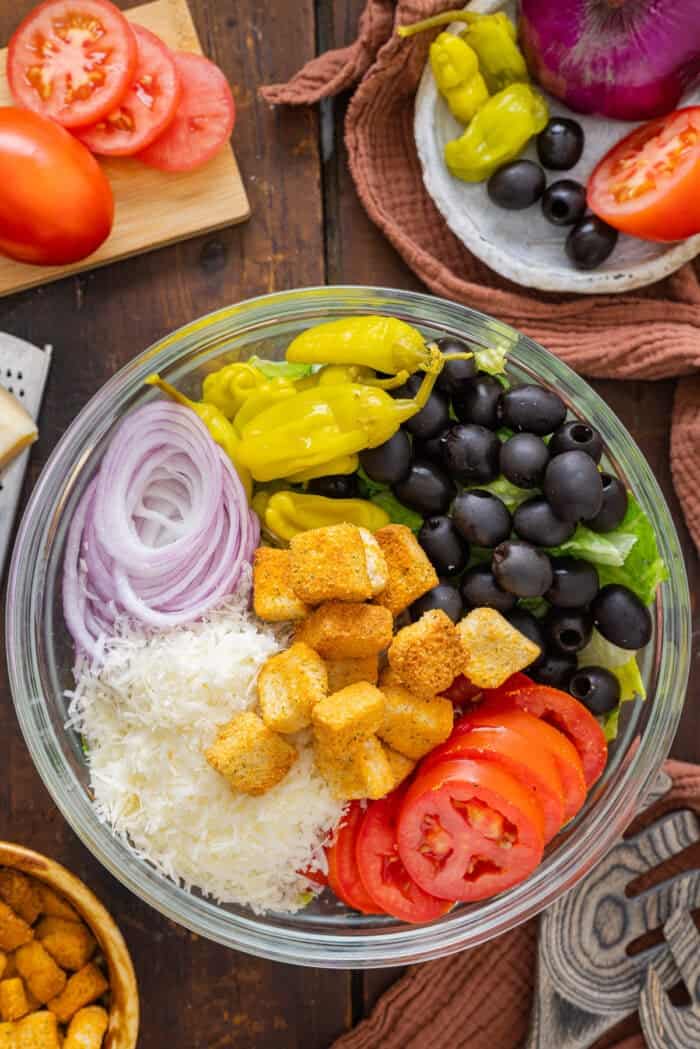 This Olive Garden Salad recipe features romaine lettuce hearts, pepperoncini, olives, and more tossed in a creamy Italian dressing. Lettuce, pepperoncini, olives, onion, Parmesan, croutons, and tomatoes in a bowl