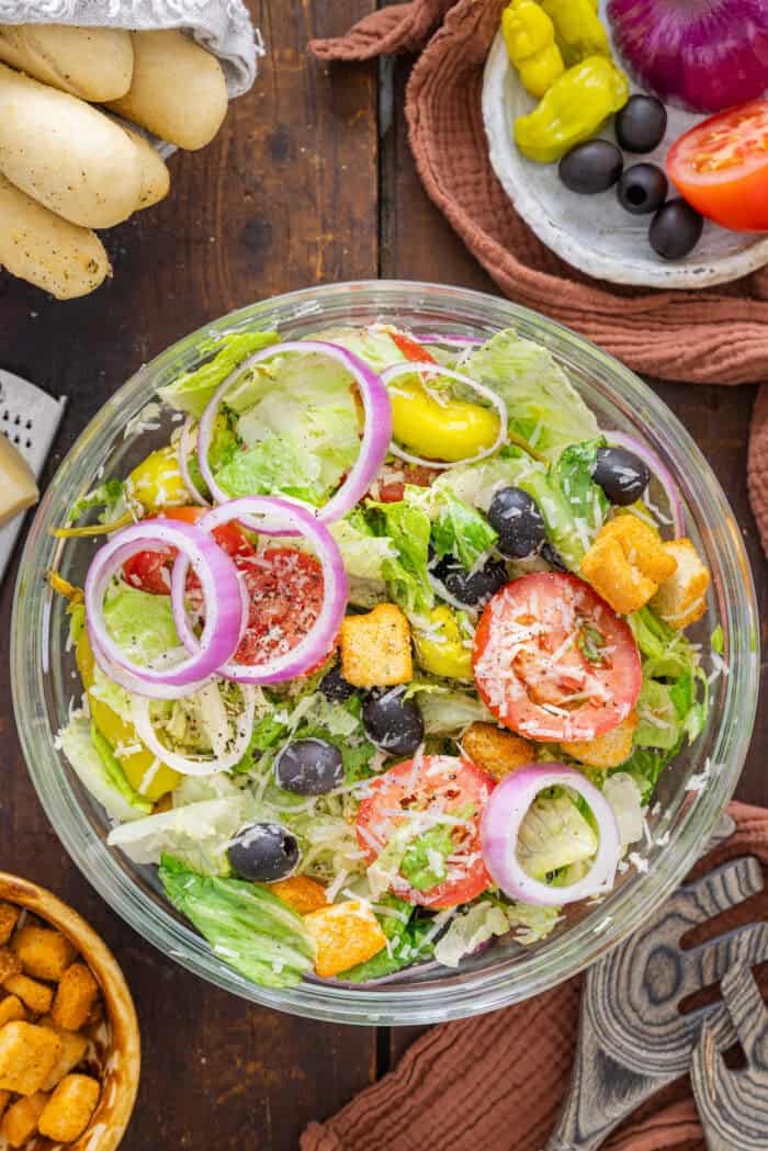 This Olive Garden Salad recipe features romaine lettuce hearts, pepperoncini, olives, and more tossed in a creamy Italian dressing. Overhead view of a bowl of Olive Garden salad