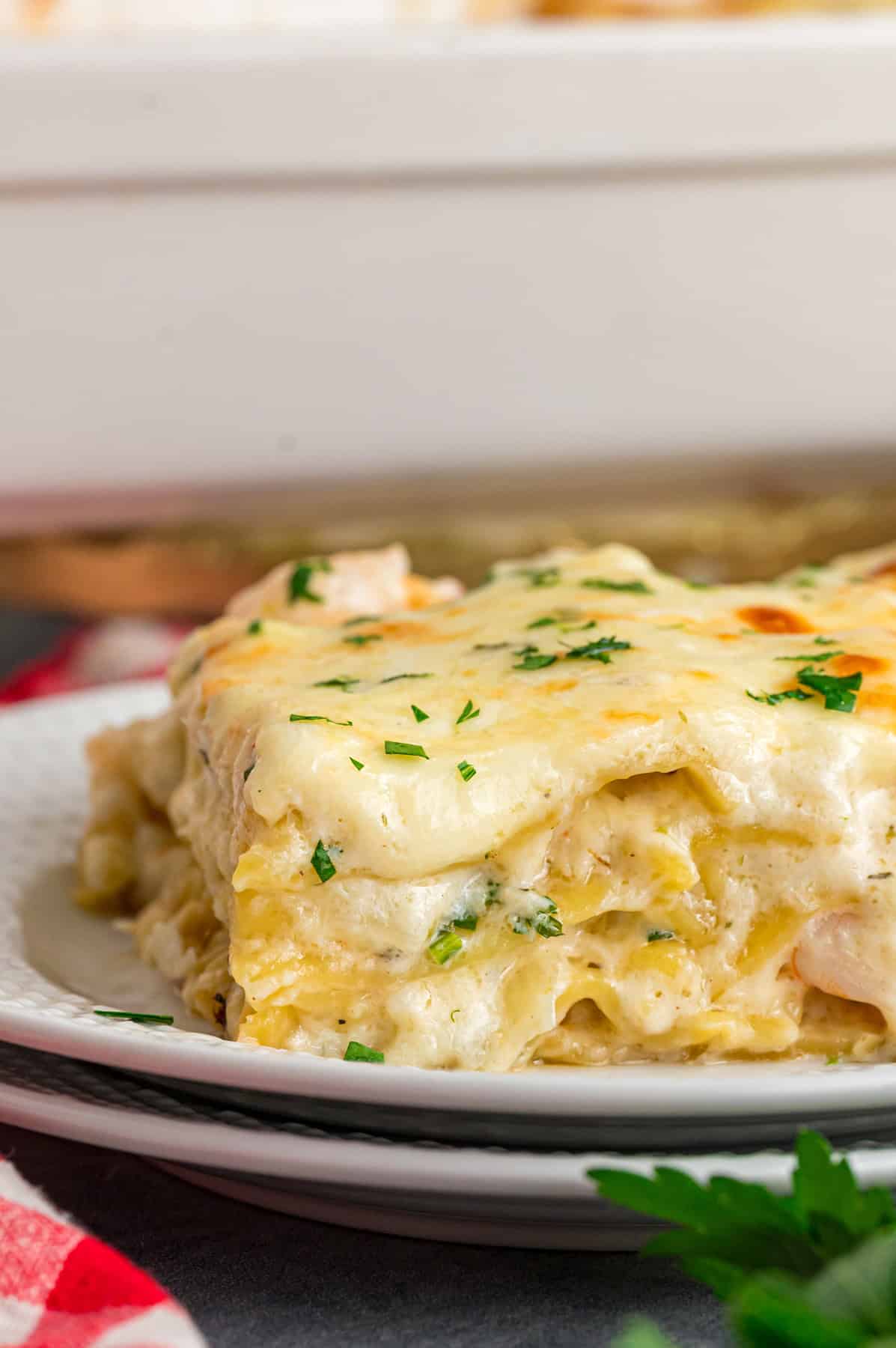This Seafood Lasagna features layers of a creamy sauce infused with clam juice, noodles, and a shrimp and crab meat filling. A plate with a slice of seafood lasagna