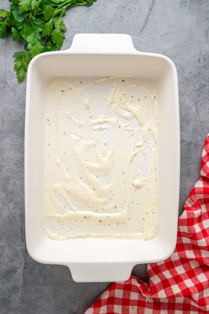 This Seafood Lasagna features layers of a creamy sauce infused with clam juice, noodles, and a shrimp and crab meat filling. Cream sauce spread in the bottom of a pan