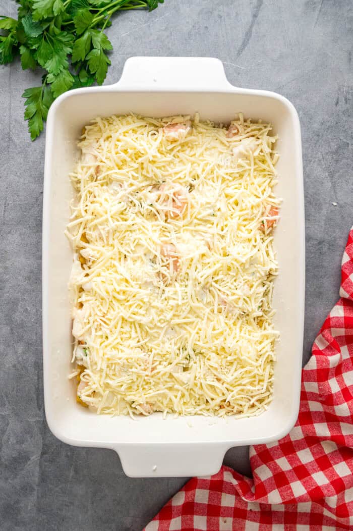 This Seafood Lasagna features layers of a creamy sauce infused with clam juice, noodles, and a shrimp and crab meat filling. Cheese on top of seafood filling in a pan