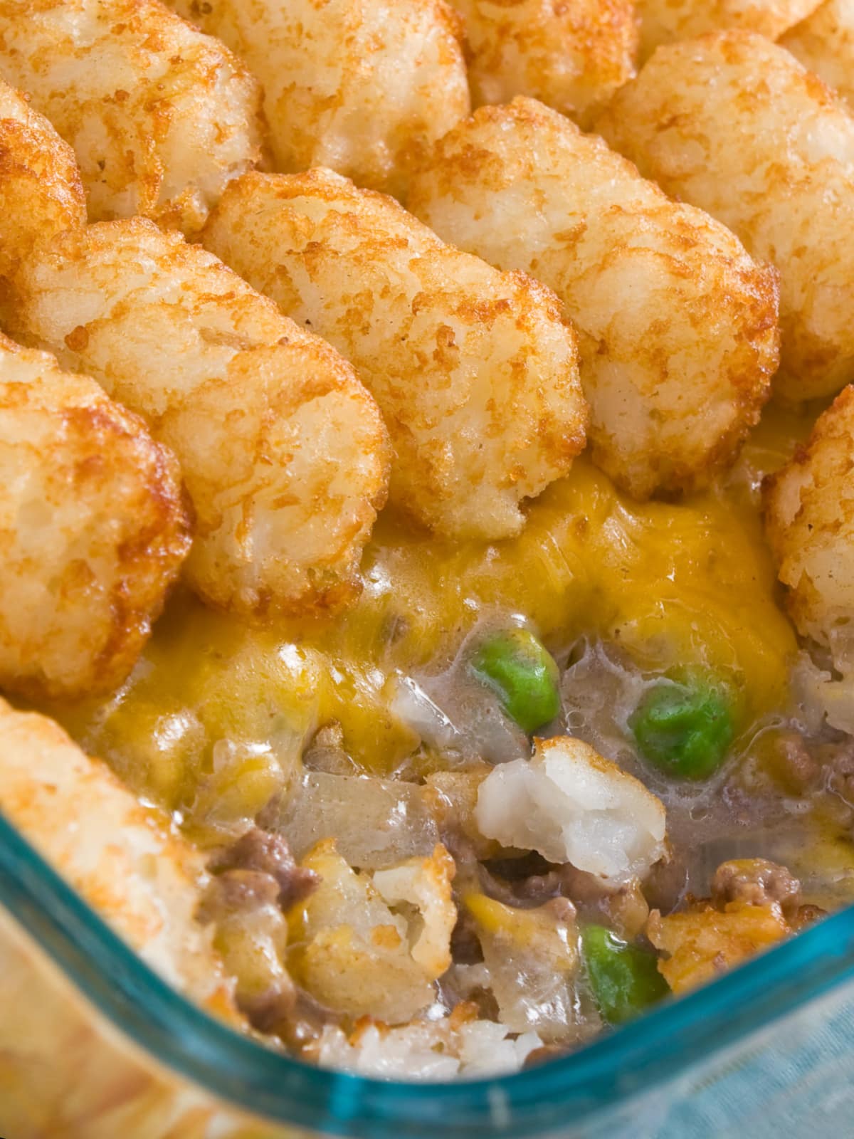 This is easy tater tot casserole recipe is always a hit! Made with ground beef, green beans, creamy soup, tater tots, and lots of cheese. clow up of Tater Tot Casserole