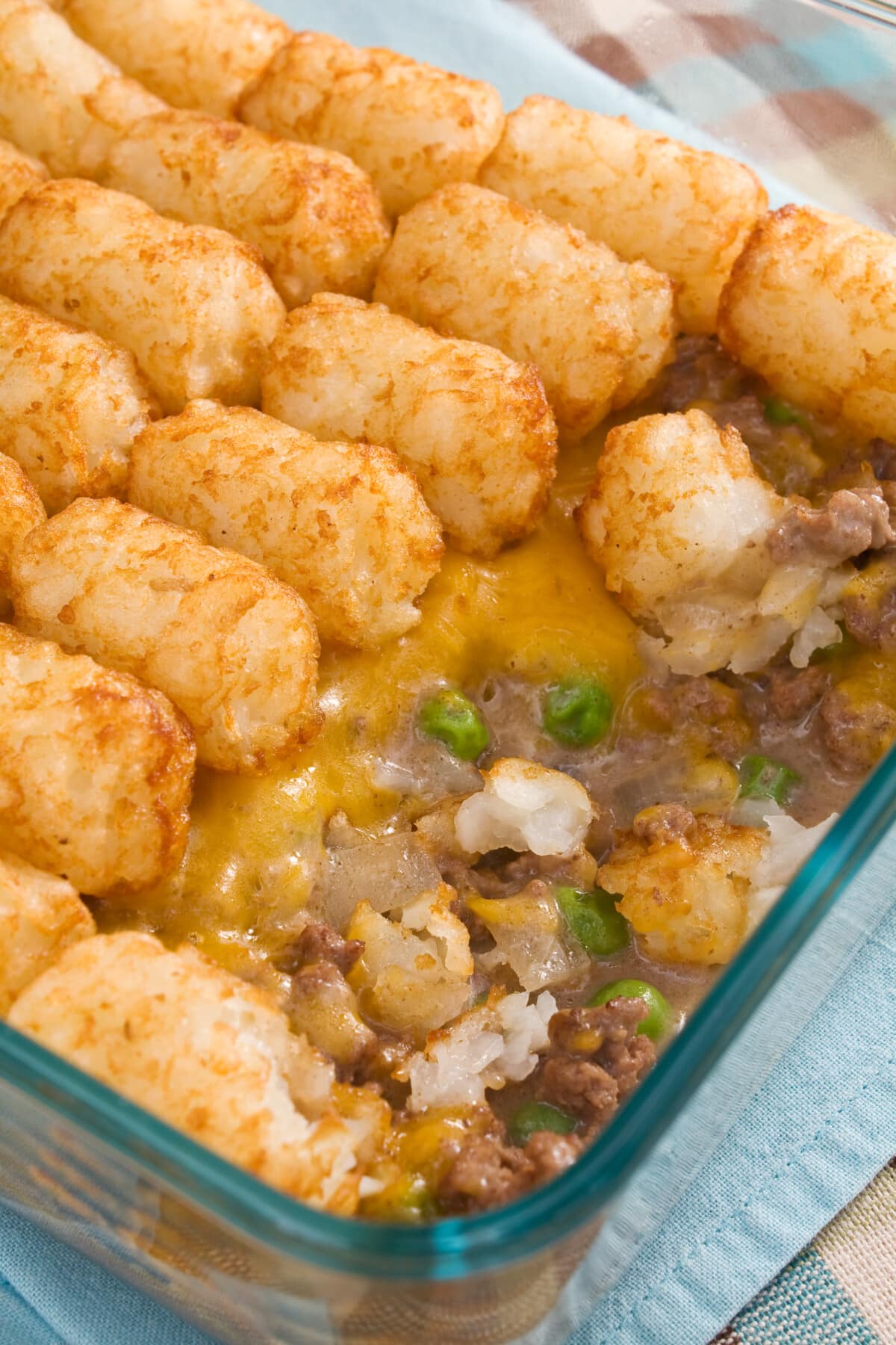This is easy tater tot casserole recipe is always a hit! Made with ground beef, green beans, creamy soup, tater tots, and lots of cheese. Tater Tot Casserole in a glass baking dish