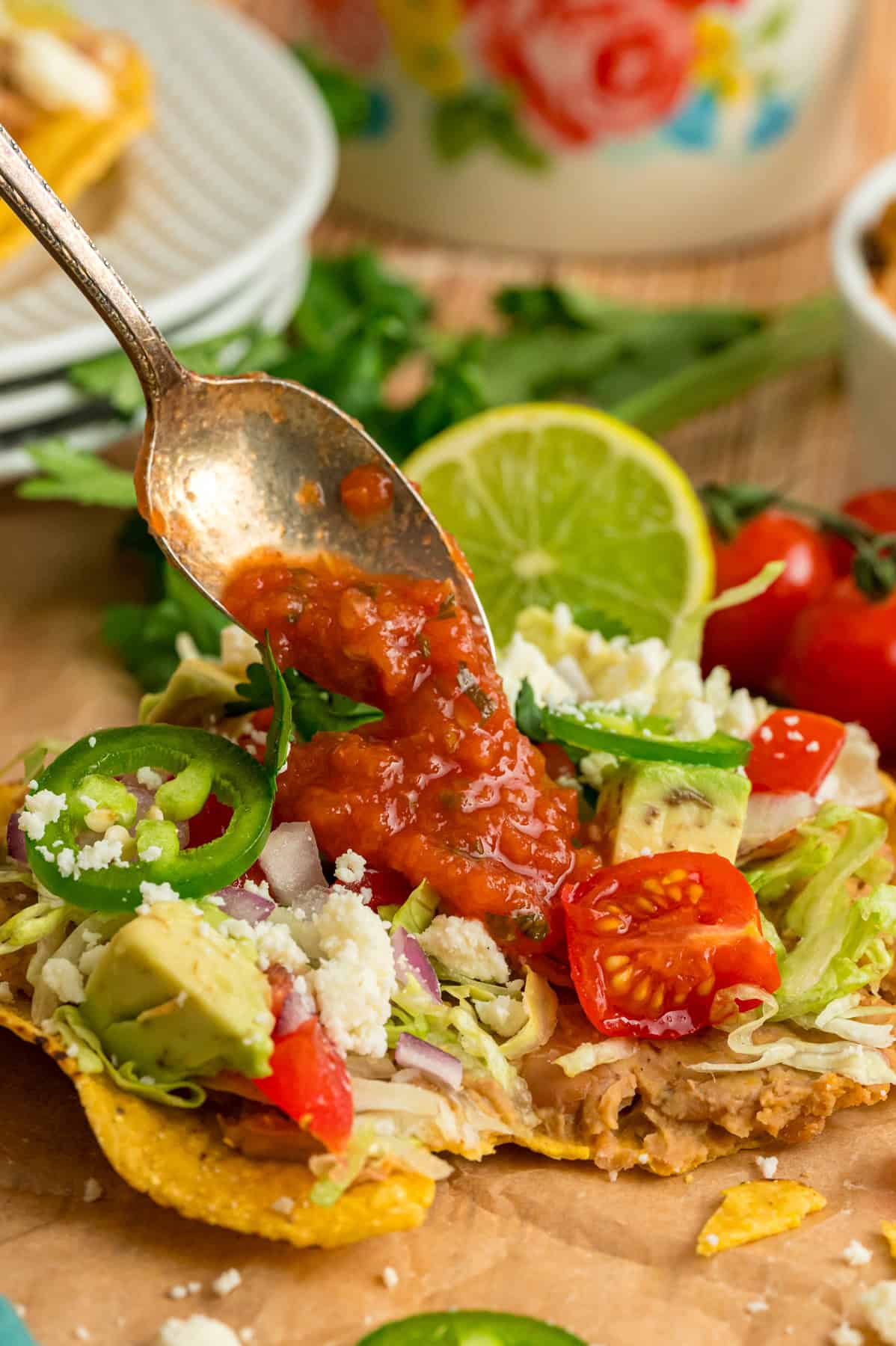 Crunchy tostada shells are topped with homemade refried beans, veggies, avocado, and cheese in this easy Tostada Recipe. Spooning salsa over an easy tostada recipe