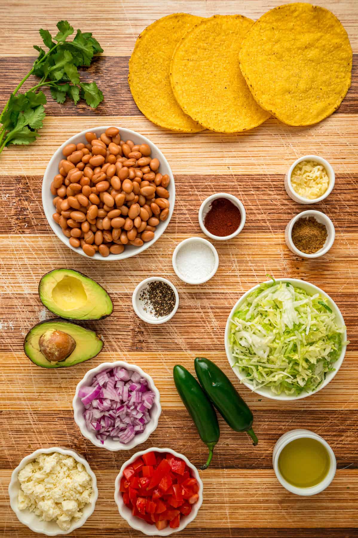 Crunchy tostada shells are topped with homemade refried beans, veggies, avocado, and cheese in this easy Tostada Recipe. Overhead view of ingredients needed to make a tostada recipe