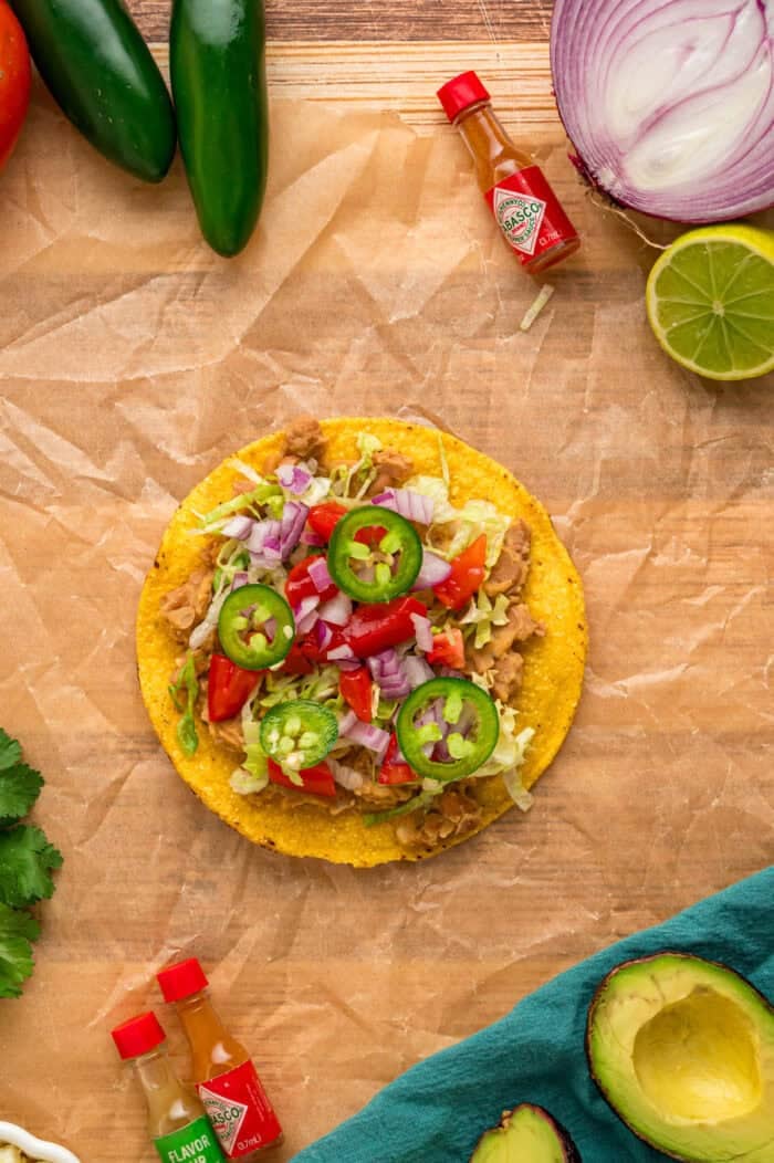 Crunchy tostada shells are topped with homemade refried beans, veggies, avocado, and cheese in this easy Tostada Recipe. Overhead view of a tostada