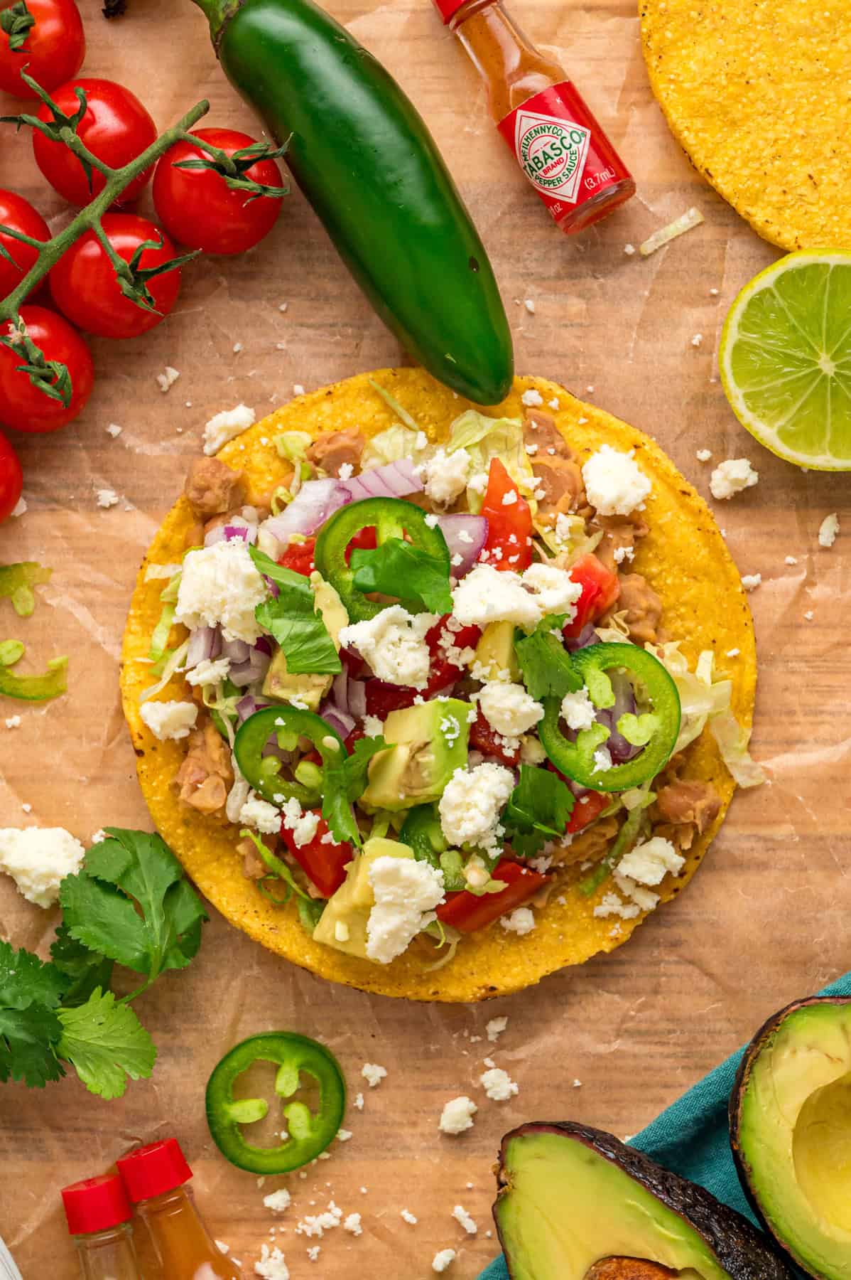 Crunchy tostada shells are topped with homemade refried beans, veggies, avocado, and cheese in this easy Tostada Recipe. Overhead view of a tostada