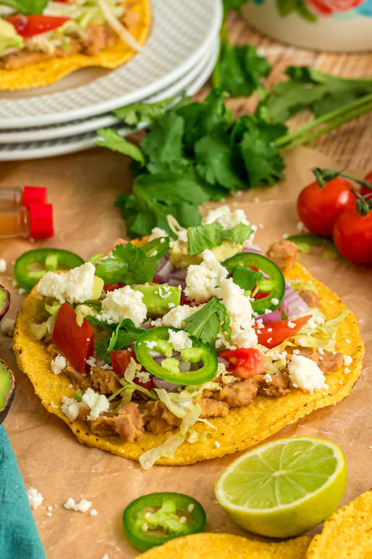 Crunchy tostada shells are topped with homemade refried beans, veggies, avocado, and cheese in this easy Tostada Recipe. A tostada on a wooden countertop